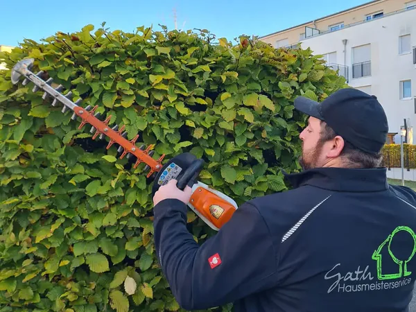 Bild von einem Gärtner der mit einer Heckenschere eine Hecke kürzt